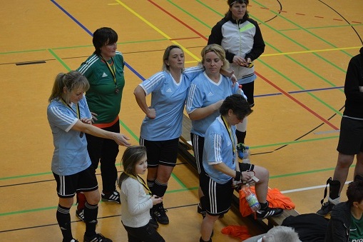 F&uuml;nf Frauen und ein M&auml;dchen stehen in Sportkleidung in einer Halle und h&ouml;ren einer Person am Rand zu.