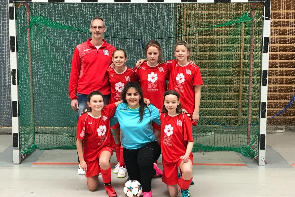 Sechser-Mannschaft fotografiert vor einem Tor: f&uuml;nf Spielerinnen in roten Trikots und ein Trainer in grauem Outfit.