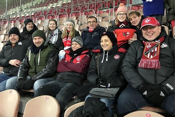 Eine Gruppe von zehn Fußballfans in Winterjacken und Schals sitzt in einem Stadion, bereit für das Spiel.