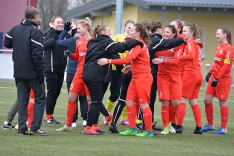 Frauenfu&szlig;ballmannschaft in roten Trikots feiert jubelnd nach dem Spiel auf einem Kunstrasenplatz.