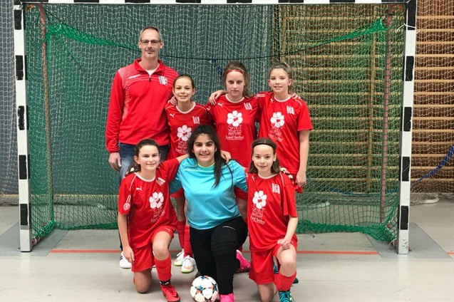 Sechser-Mannschaft fotografiert vor einem Tor: f&uuml;nf Spielerinnen in roten Trikots und ein Trainer in grauem Outfit.