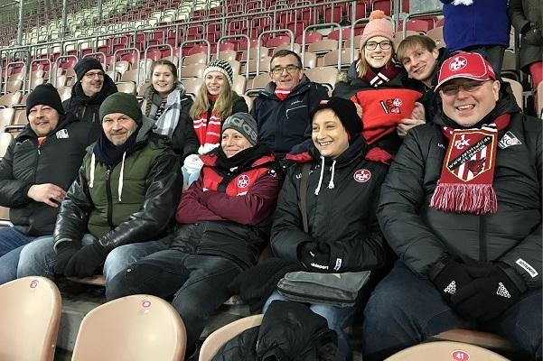 Eine Gruppe von zehn Fu&szlig;ballfans in Winterjacken und Schals sitzt in einem Stadion, bereit f&uuml;r das Spiel.