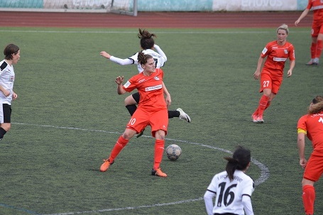 Spielszene eines Frauenfu&szlig;ballspiels: Spielerinnen in roten und schwarzen Trikots k&auml;mpfen um den Ball auf gr&uuml;nem Rasen.