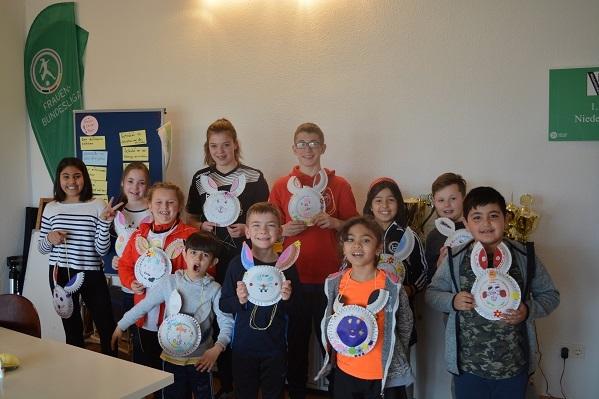 Gruppe von Kindern hält selbstgebastelte bunte Hasenmasken in einem Raum mit Ausbildungsmaterialien.