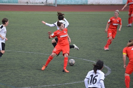 Spielszene eines Frauenfu&szlig;ballspiels: Spielerinnen in roten und schwarzen Trikots k&auml;mpfen um den Ball auf gr&uuml;nem Rasen.