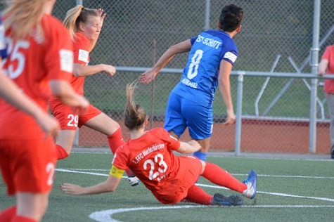 Zwei Fu&szlig;ballspielerinnen in roten Trikots, eine f&auml;llt, w&auml;hrend eine Spielerin in Blau den Ball ber&uuml;hrt.