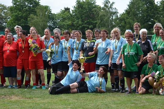 Zwei Fu&szlig;ballmannschaften mit Medaillen stehen gemeinsam auf einem Spielfeld, einige halten Pokale und Blumen.