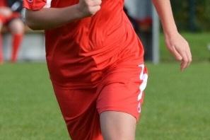 Spielende Fußballspielerin in roter Uniform sprintet über einen grünen Rasenplatz, Blick nach vorne gerichtet.