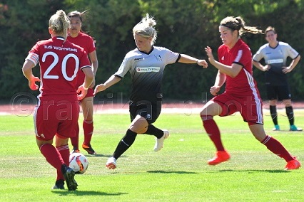 Fu&szlig;ballspiel: Eine Spielerin in Schwarz dribbelt, w&auml;hrend zwei Gegnerinnen in Rot versuchen, sie zu stoppen.