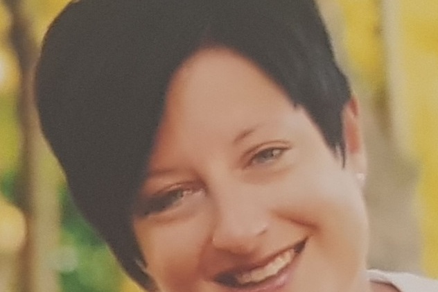 Portr&auml;t einer l&auml;chelnden Frau mit dunklem, kurzem Haar und hellen Kleidungsst&uuml;cken vor unscharfem, farbenfrohem Hintergrund.