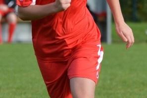 Spielende Fu&szlig;ballspielerin in roter Uniform sprintet &uuml;ber einen gr&uuml;nen Rasenplatz, Blick nach vorne gerichtet.