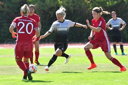 Fu&szlig;ballspiel: Eine Spielerin in Schwarz dribbelt, w&auml;hrend zwei Gegnerinnen in Rot versuchen, sie zu stoppen.