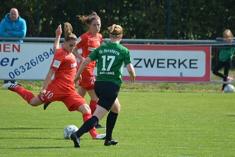 Zwei Fu&szlig;ballspielerinnen stehen sich gegen&uuml;ber, eine in rotem Trikot kickt den Ball, die andere in gr&uuml;nem Trikot ist bereit.