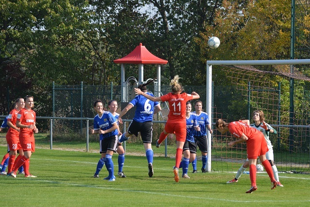 Frauenfu&szlig;ballspiel: Eine Spielerin springt, um einen Ball im Strafraum zu k&ouml;pfen, w&auml;hrend andere Spielerinnen darauf reagieren.