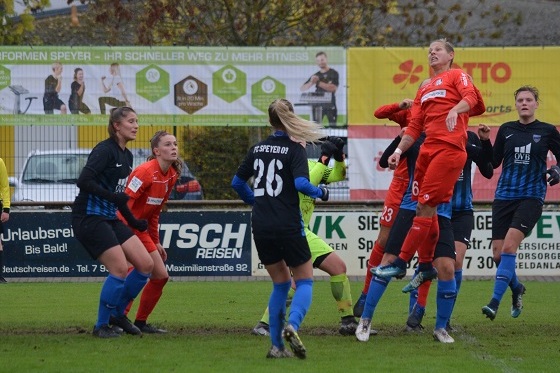 Spielszene im Frauenfu&szlig;ball mit aktiven Spielerinnen, die um den Ball in der Luft k&auml;mpfen, im Hintergrund Werbebanner.