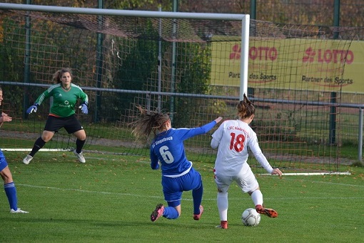 Zwei Spielerinnen in Aktion auf dem Fu&szlig;ballplatz, eine in blauem, die andere in wei&szlig;em Trikot, Ball am Fu&szlig;.