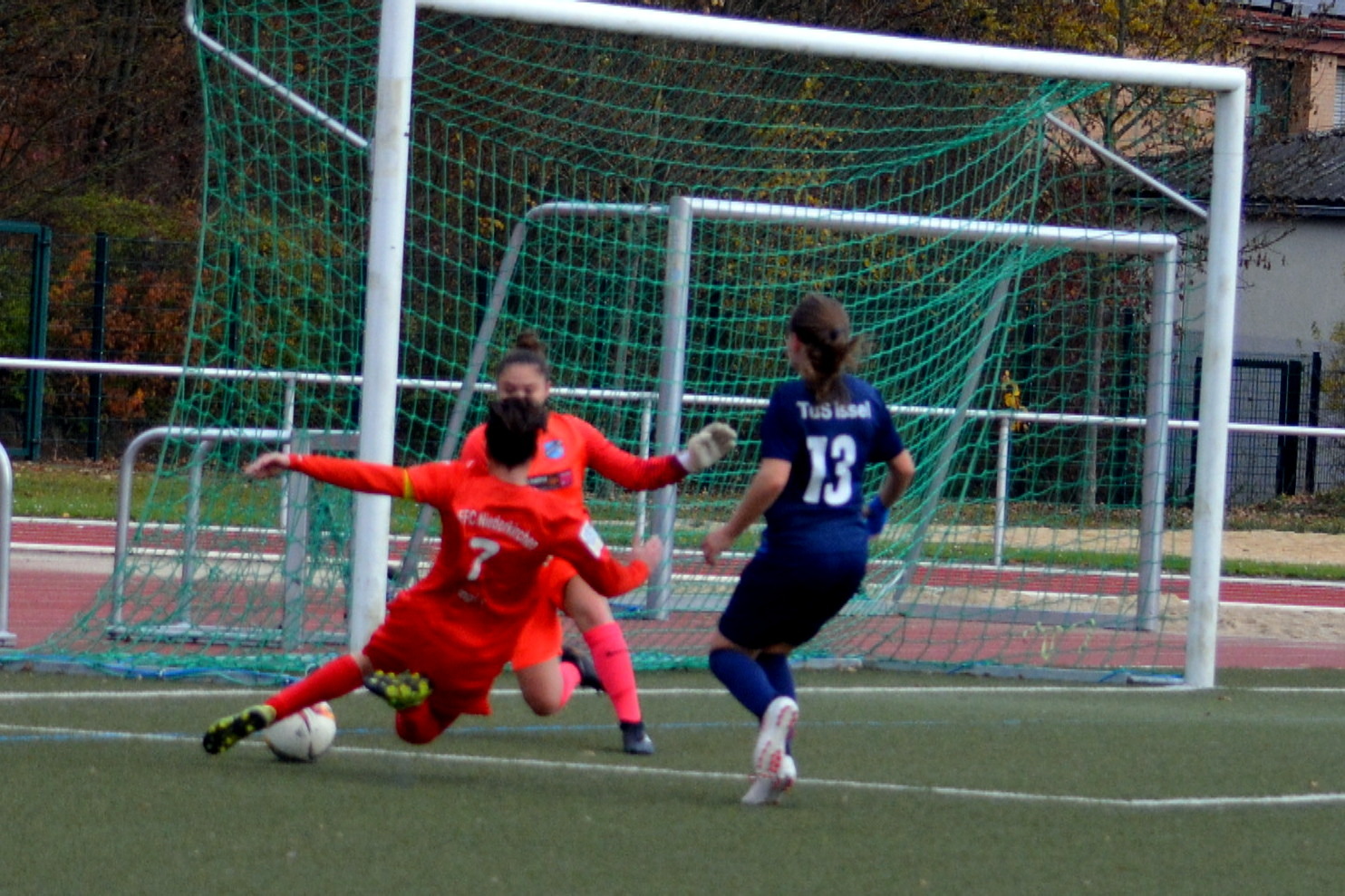 Torh&uuml;terin in rotem Trikot rettet den Ball beim Spiel gegen eine Spielerin in blauem Trikot auf dem Fu&szlig;ballplatz.