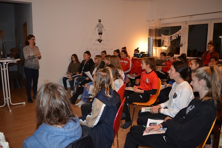 Eine Gruppe junger Frauen sitzt in einem Raum und h&ouml;rt einer Rednerin aufmerksam zu.