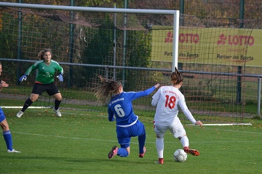 Zwei Spielerinnen in Aktion auf dem Fu&szlig;ballplatz, eine in blauem, die andere in wei&szlig;em Trikot, Ball am Fu&szlig;.