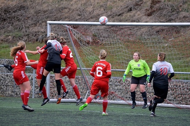 Fu&szlig;ballspiel mit spielenden Frauen, die zu einem hohen Ball im Tor springen, w&auml;hrend die Torh&uuml;terin beobachtet.