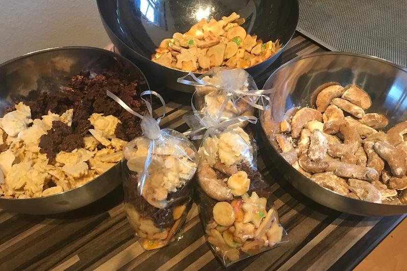 Drei Schalen mit verschiedenen Keksen und zwei durchsichtigen Tüten mit Naschereien auf einem Holzuntergrund.