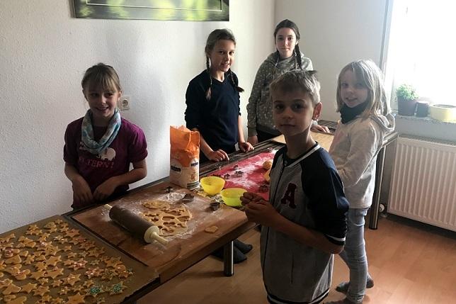 Kinder backen gemeinsam Plätzchen an einem Tisch, umgeben von Zutaten und ausgestochenen Keksen.