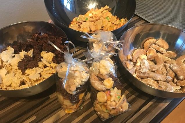 Drei Schalen mit verschiedenen Keksen und zwei durchsichtigen T&uuml;ten mit Naschereien auf einem Holzuntergrund.