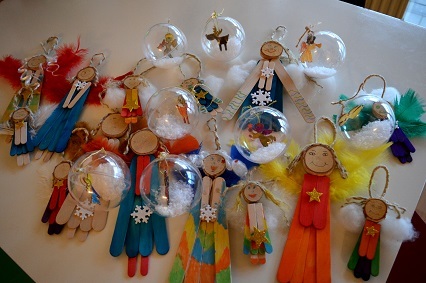 Bunte handgefertigte Weihnachtsanh&auml;nger aus Holz, Perlen und Federn in verschiedenen Formen und Farben auf einem Tisch.