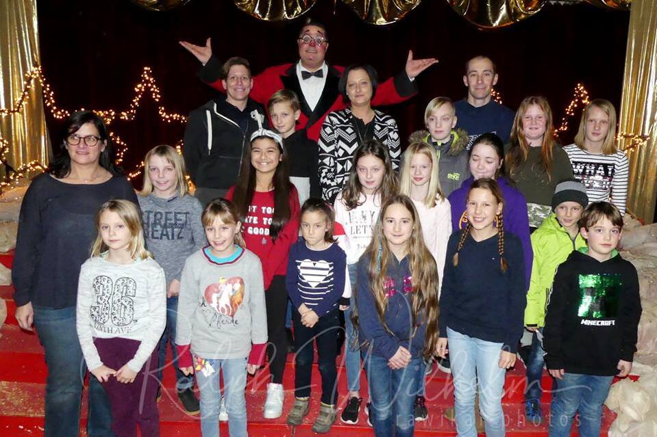 Gruppe von Kindern und Erwachsenen posiert vor einer festlichen Kulisse mit Lichtern und rotem Teppich.