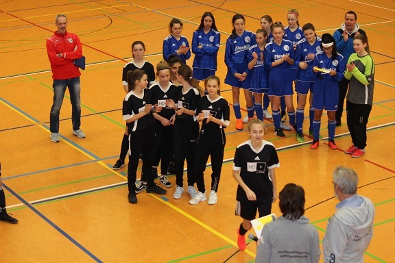 Zwei Gruppen von Fu&szlig;ballspielerinnen in Schwarz und Blau stehen in einer Sporthalle, w&auml;hrend eine Zeremonie stattfindet.