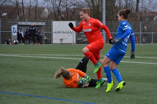 Zwei Spielerinnen im blauen und roten Trikot k&auml;mpfen um den Ball; eine Torh&uuml;terin liegt am Boden.