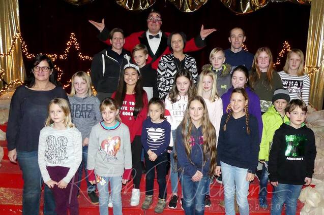 Gruppe von Kindern und Erwachsenen posiert vor einer festlichen Kulisse mit Lichtern und rotem Teppich.