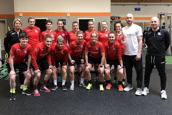 Gruppenfoto einer Fu&szlig;ballmannschaft in roten Trikots, stehend im Fitnessstudio mit Trainern.