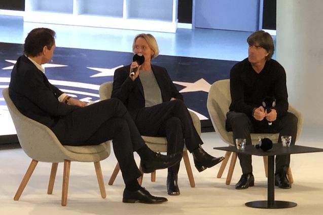 Drei Personen sitzen in modernen St&uuml;hlen in einem hellen Raum und diskutieren, Mikrofone in der Hand.