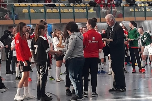 M&auml;dchenfu&szlig;ballspielerinnen stehen auf einem Hallenplatz und empfangen Preise von einem Ehrenamtlichen in Anzug.
