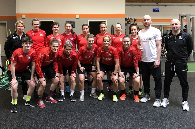 Gruppenfoto einer Fu&szlig;ballmannschaft in roten Trikots, stehend im Fitnessstudio mit Trainern.