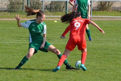 Zwei Fu&szlig;ballspielerinnen in Aktion, eine tr&auml;gt gr&uuml;ne und die andere rote Trikots, auf einem Rasenfeld.
