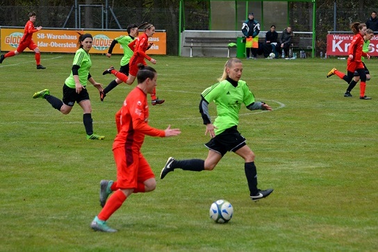 Fu&szlig;ballspiel mit Spielerinnen in gr&uuml;nen und roten Trikots auf einem Rasenplatz, Ball im Spiel.