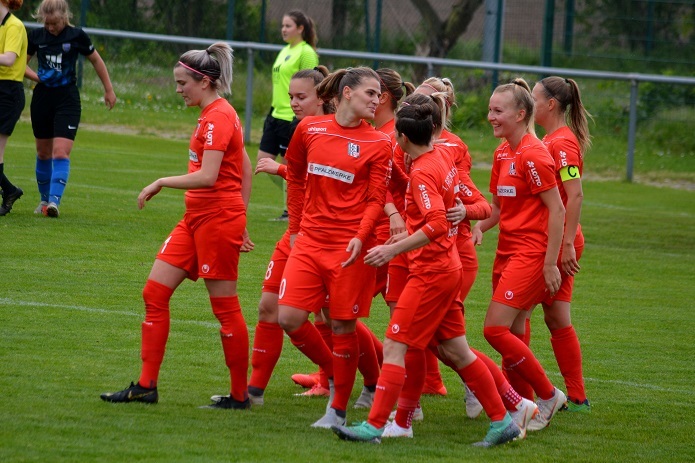 Gruppenkonferenz von Spielerinnen in roten Trikots auf dem Fu&szlig;ballplatz, jubelnd nach einem Tor.