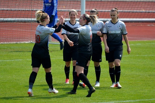 Sechs Fu&szlig;ballspielerinnen in schwarz-wei&szlig;en Trikots feiern gemeinsam ein Tor auf dem Spielfeld.