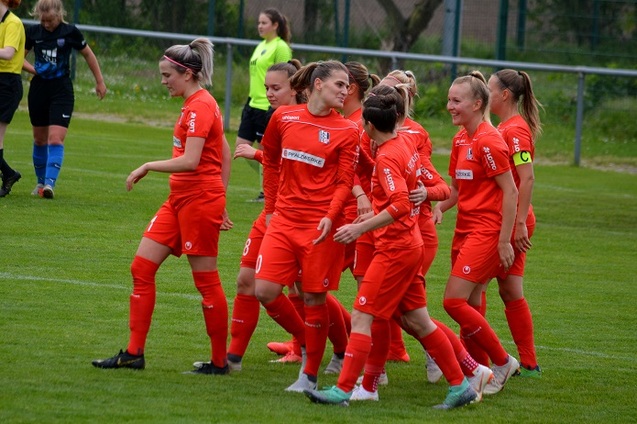 Gruppenkonferenz von Spielerinnen in roten Trikots auf dem Fu&szlig;ballplatz, jubelnd nach einem Tor.