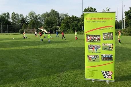 Gruppentraining von Fu&szlig;ballerinnen auf dem Platz, ein Werbebanner des 1. FFC 08 Niederkirchen im Vordergrund.