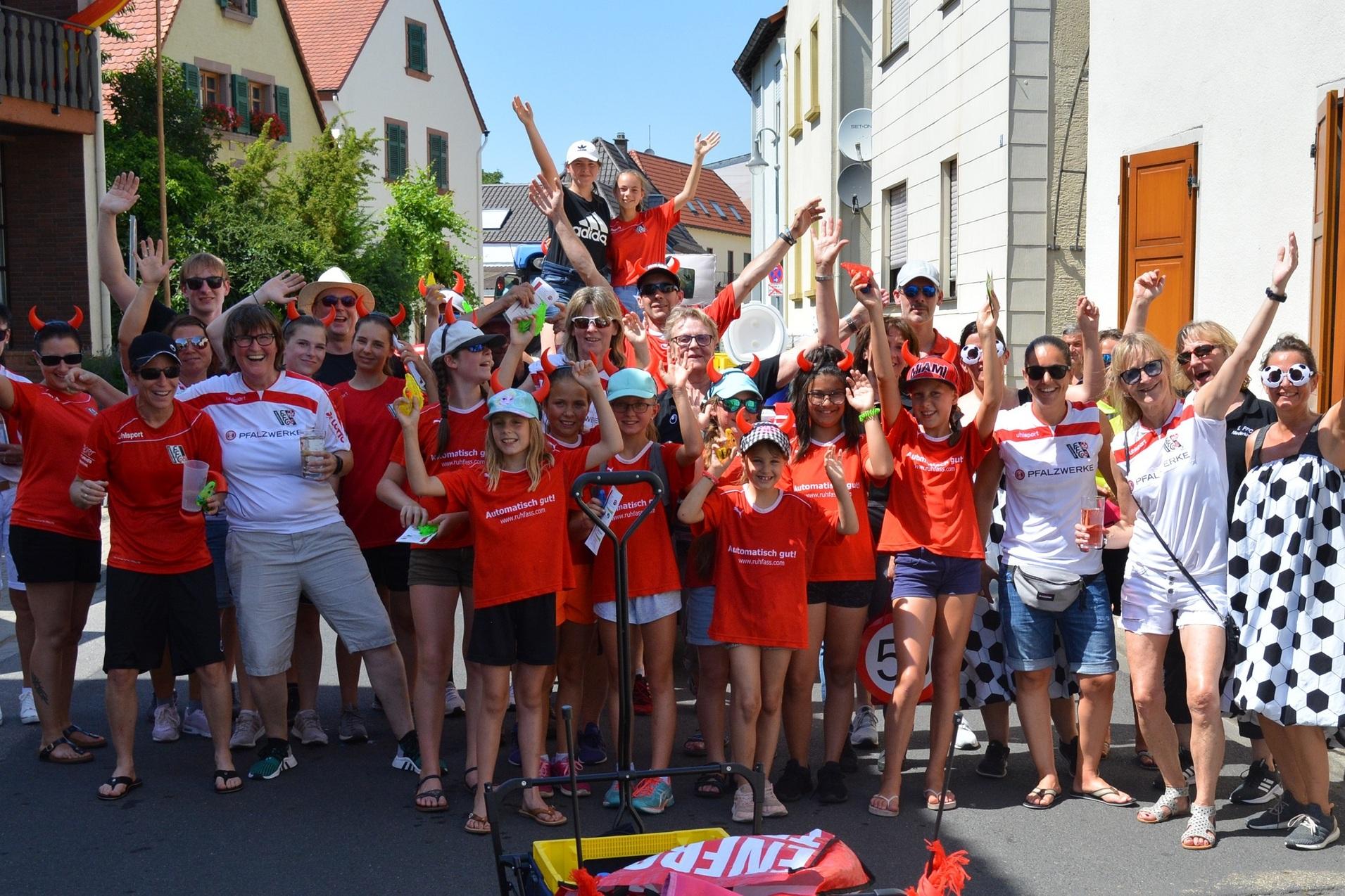 Gruppenshot von festlichen Menschen in roten T-Shirts, die fr&ouml;hlich auf einer Stra&szlig;e stehen und die H&auml;nde erheben.