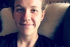 Nahaufnahme einer Person mit l&auml;chelndem Gesicht, die auf einem Sessel mit einem hellen, weichen Bezug sitzt.