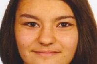 Porträt einer lächelnden jungen Frau mit langen, glatten Haaren und neutralem Hintergrund.