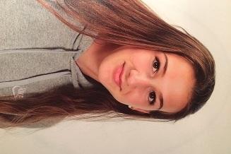 Portr&auml;t eines M&auml;dchens mit langen, braunen Haaren, das in einem grauen Hoodie freundlich in die Kamera schaut.