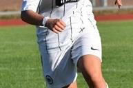 Eine Fu&szlig;ballspielerin in wei&szlig;em Trikot l&auml;uft mit dem Ball auf einem gr&uuml;nen Rasenplatz.