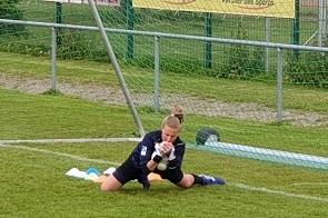 Torh&uuml;terin liegt auf dem Spielfeld und f&auml;ngt den Ball, w&auml;hrend ihre Ausr&uuml;stung auf dem Gras liegt.
