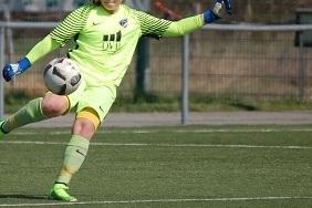 Torh&uuml;terin im gelben Dress kickt einen Fu&szlig;ball auf einem gr&uuml;nen Kunstrasenplatz.