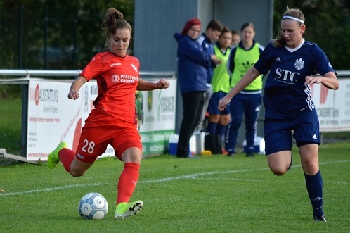 Spielerin in rotem Trikot dribbelt den Ball auf dem Fu&szlig;ballfeld, w&auml;hrend eine Gegnerin sie verfolgt.